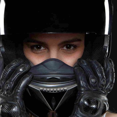 Beautiful young woman in black leather gloves and protective motorbike helmet in studio. Attractive self determined female motocycle racer wearing hands and body protection from falls and accidents